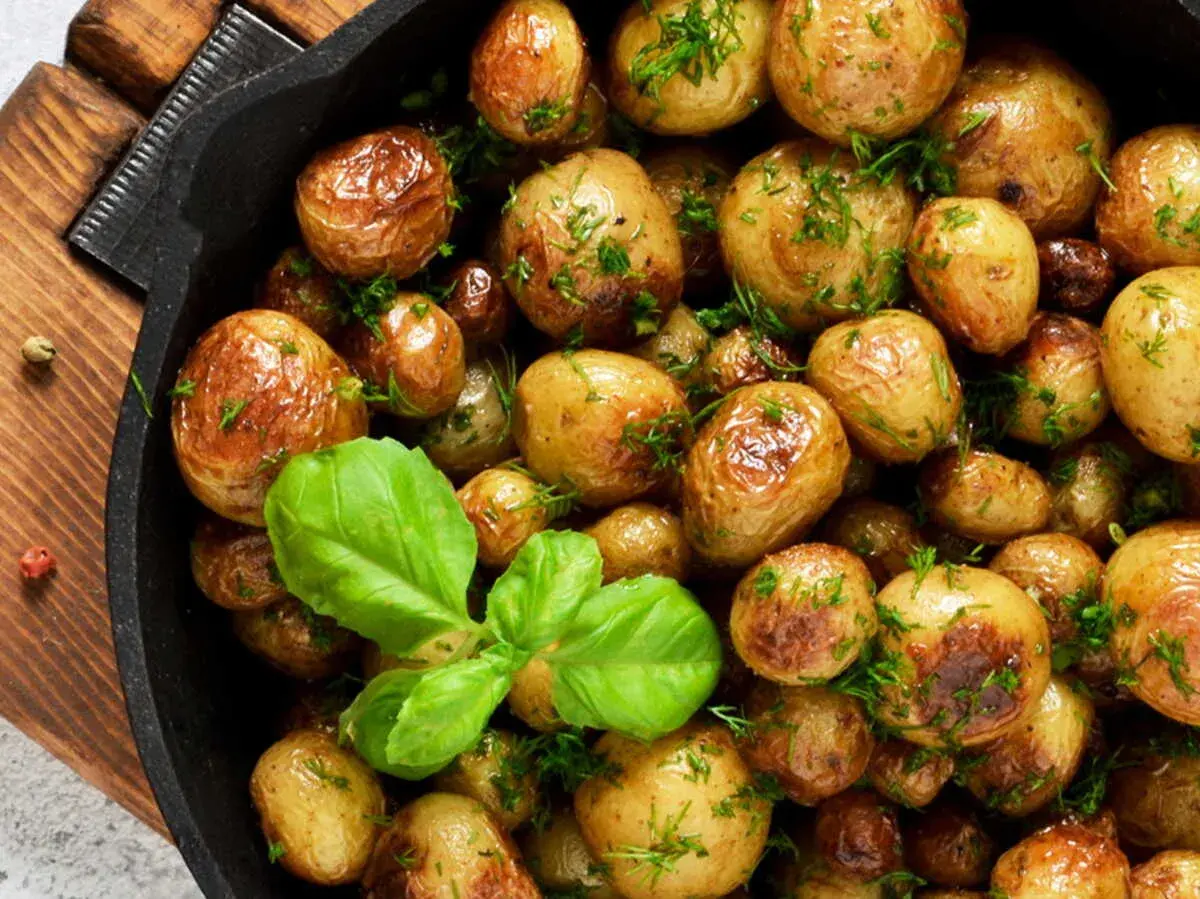 Poêlée de pommes de terre grenaille dorées et parsemées d'herbes fraîches, avec une feuille de basilic.