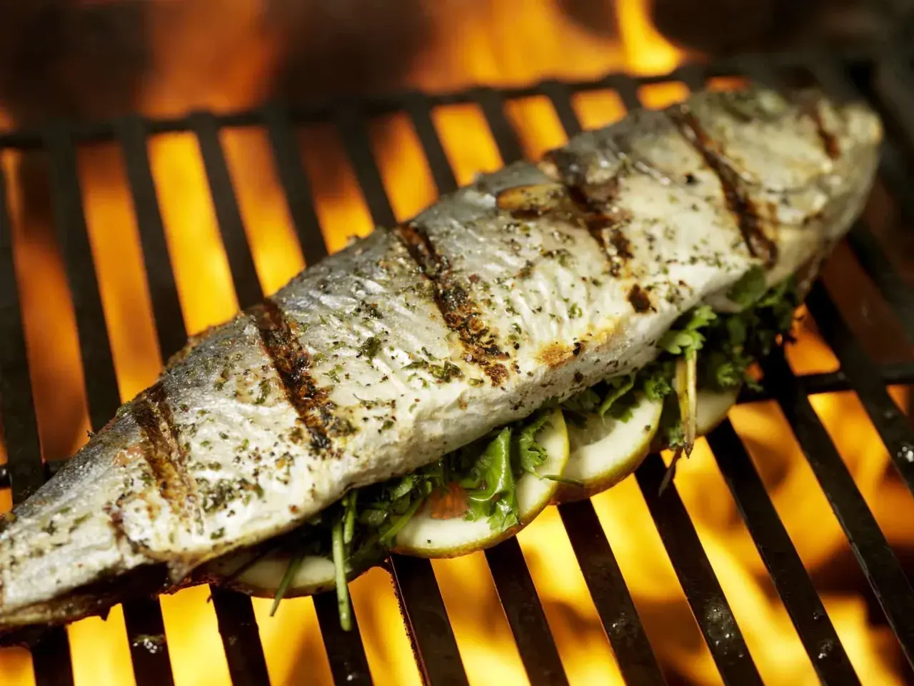 Poisson entier assaisonné, garni de tranches de citron et d'herbes, cuisant sur un gril avec des flammes vives en arrière-plan. Un délice de thon au barbecue.