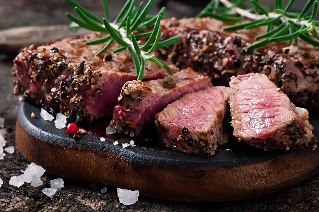 Un succulent filet mignon basse température, coupé en tranches, garni de romarin et de poivre concassé, sur une planche en bois rustique.