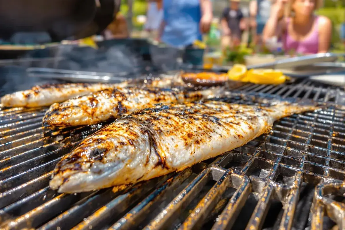 Trois poissons entiers, marqués par le barbecue, grillent sur une grille. Des éclats de citron sont visibles en arrière-plan.