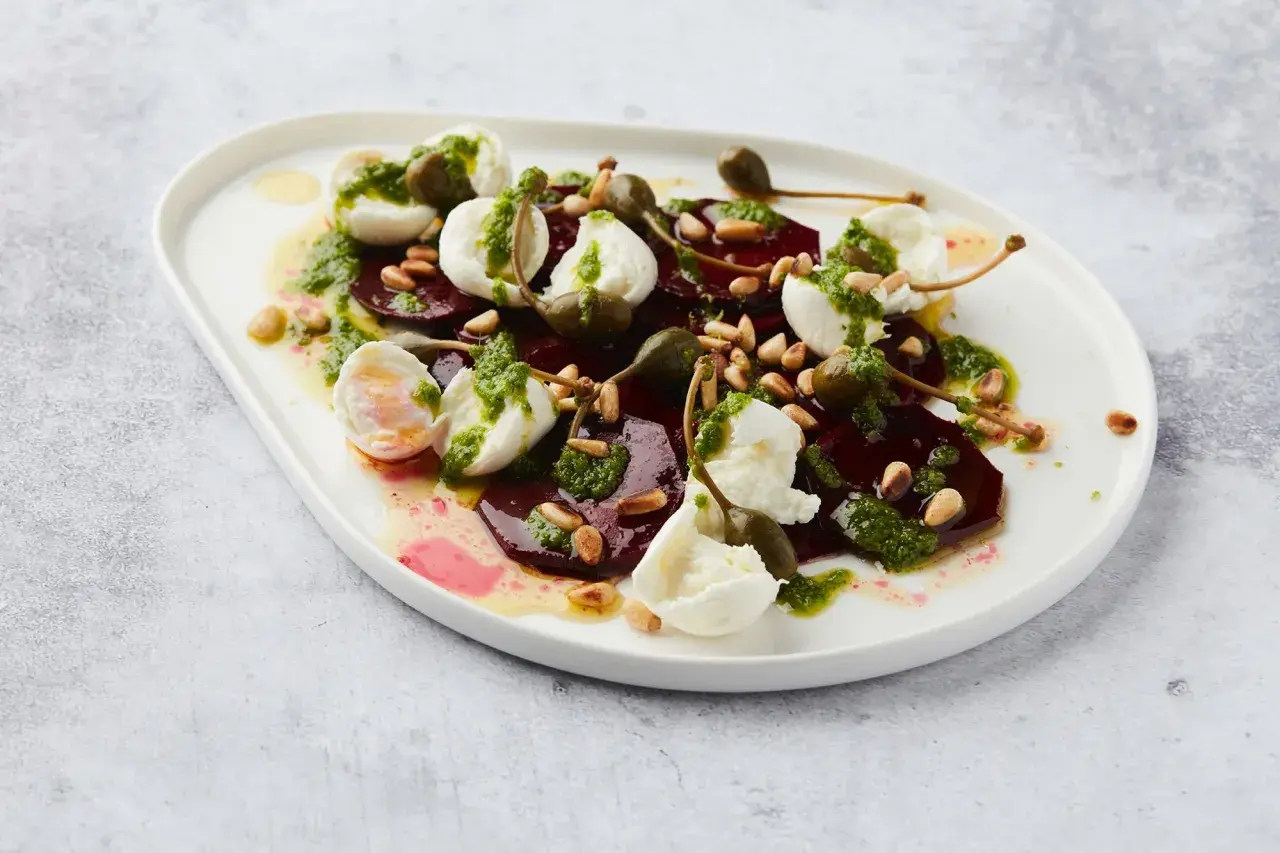 Salade de betterave fumée, mozzarella, pignons et câpres, arrosée d'une sauce verte.