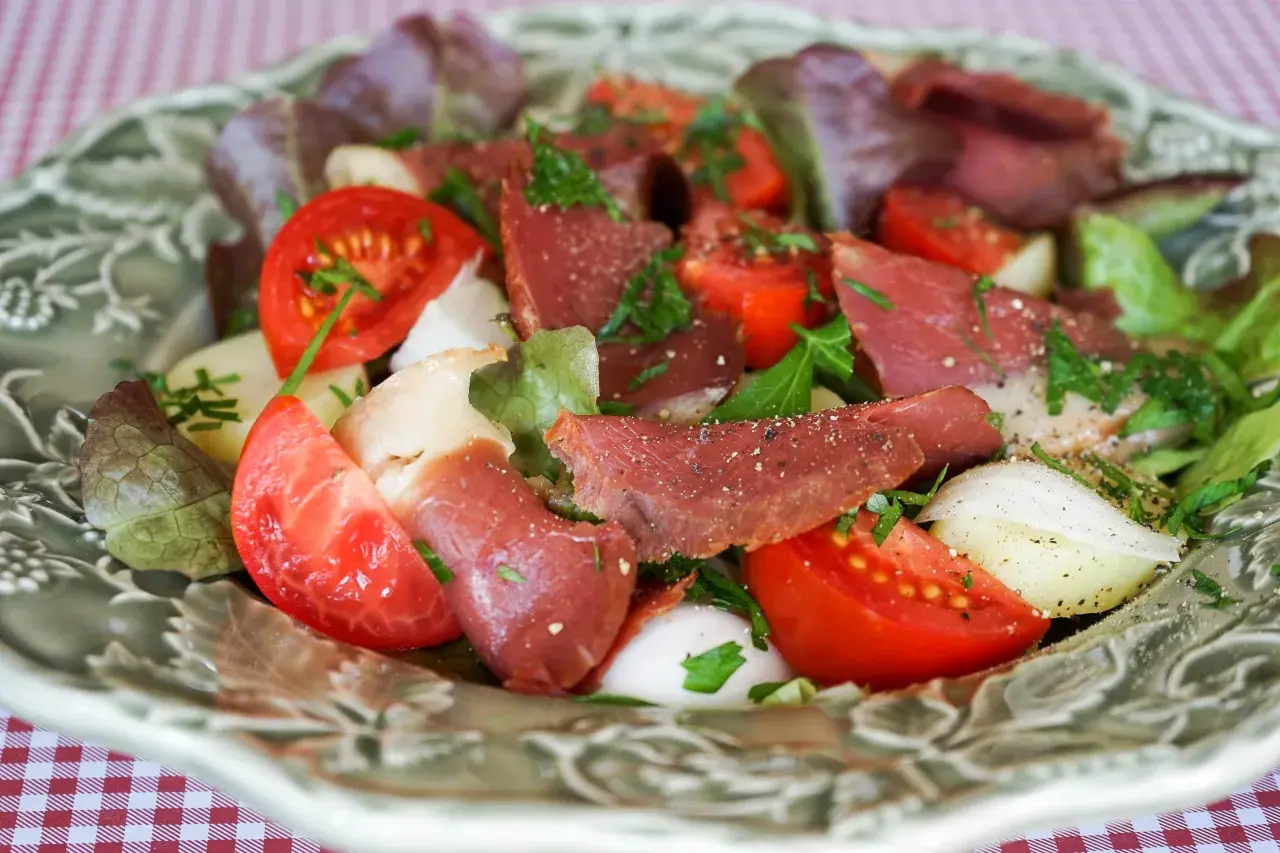 Salade fraîche avec des tranches de fumer magret de canard, tomates, oignons et laitue, parsemée d'herbes.