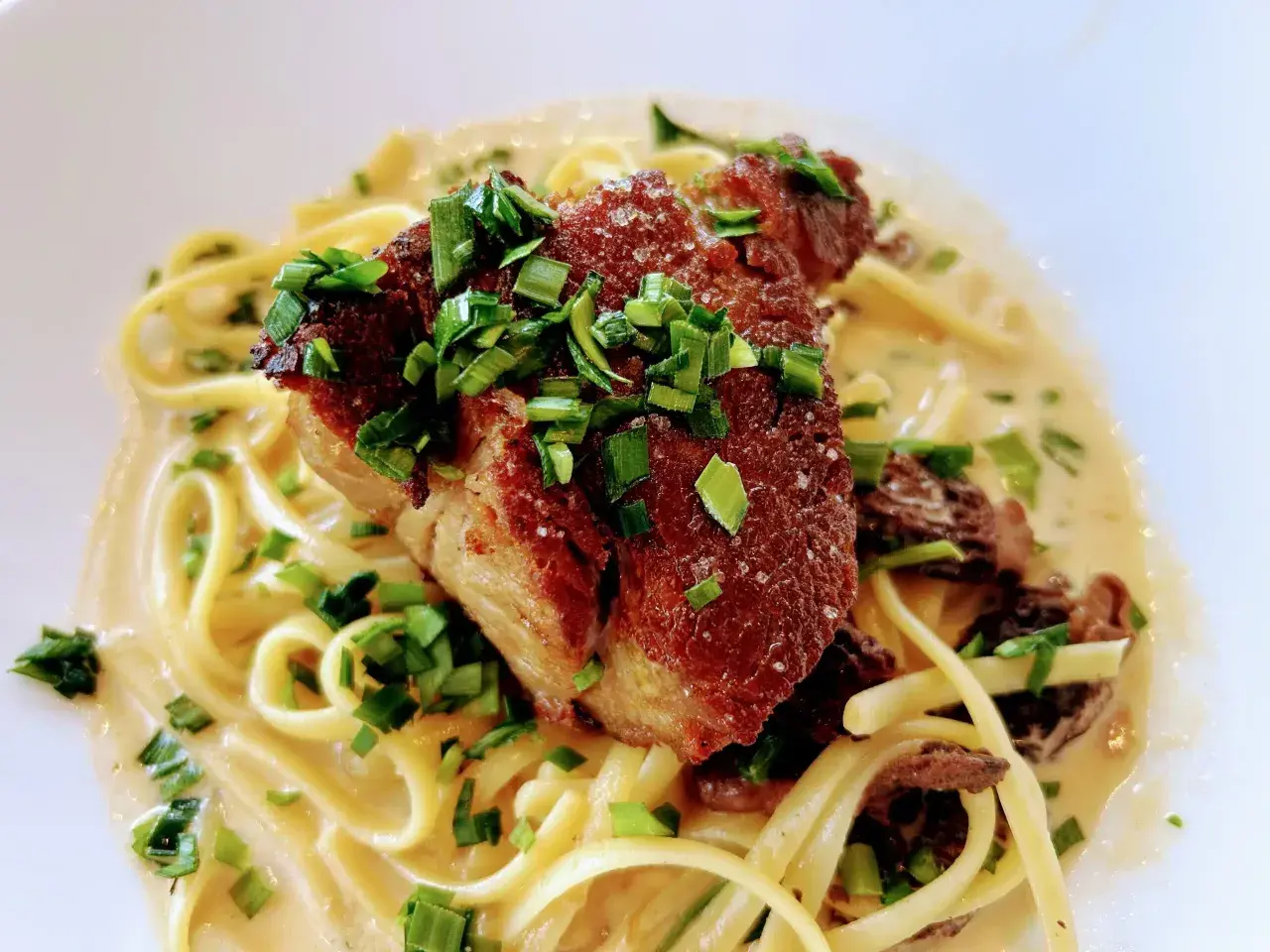 Un morceau d'échine de porc croustillante sur des pâtes crémeuses, garni de ciboule fraîche. Un délice !