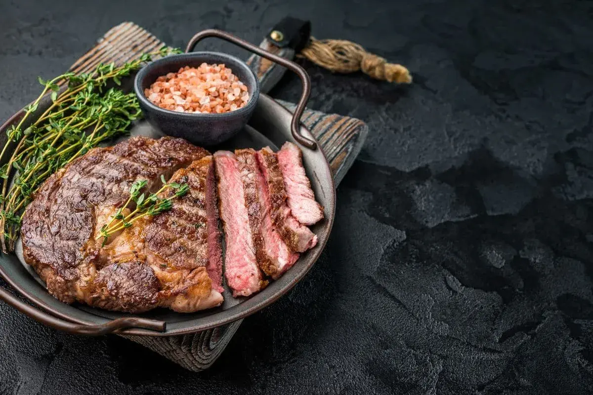 Un succulent entrecôte grillé, tranché et garni de thym frais, servi avec du sel rose sur un plateau.