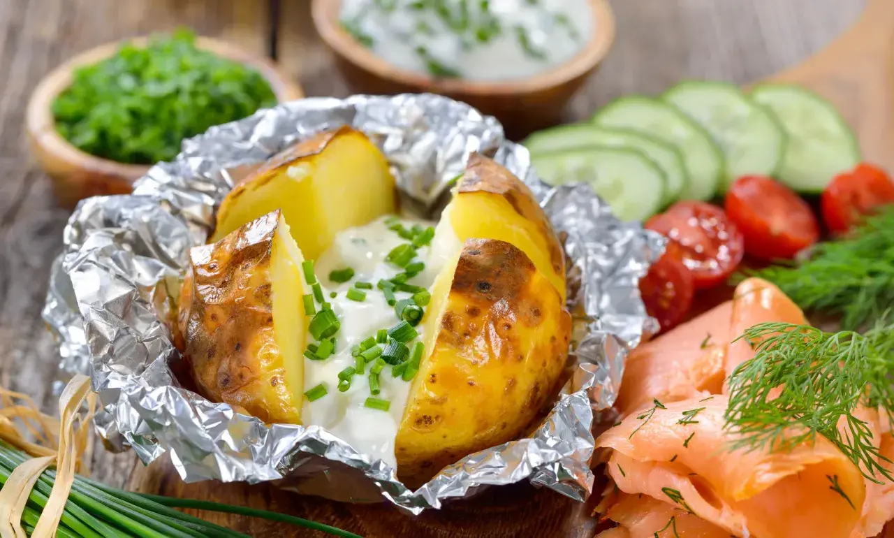 Pommes de terre à la braise, enveloppées dans du papier aluminium, garnies de crème et de ciboulette. Parfait pour le temps de cuisson.