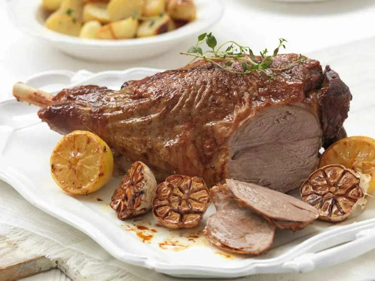 Gigot d'agneau rôti, parfumé au thym, servi avec des citrons grillés et de l'ail confit. Parfait pour une cuisson agneau barbecue réussie.