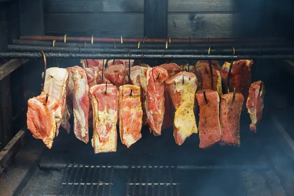 Viande crue assaisonnée suspendue dans un fumoir, prête pour le fumage. Le fumoir est alimenté par une bouteille de gaz.