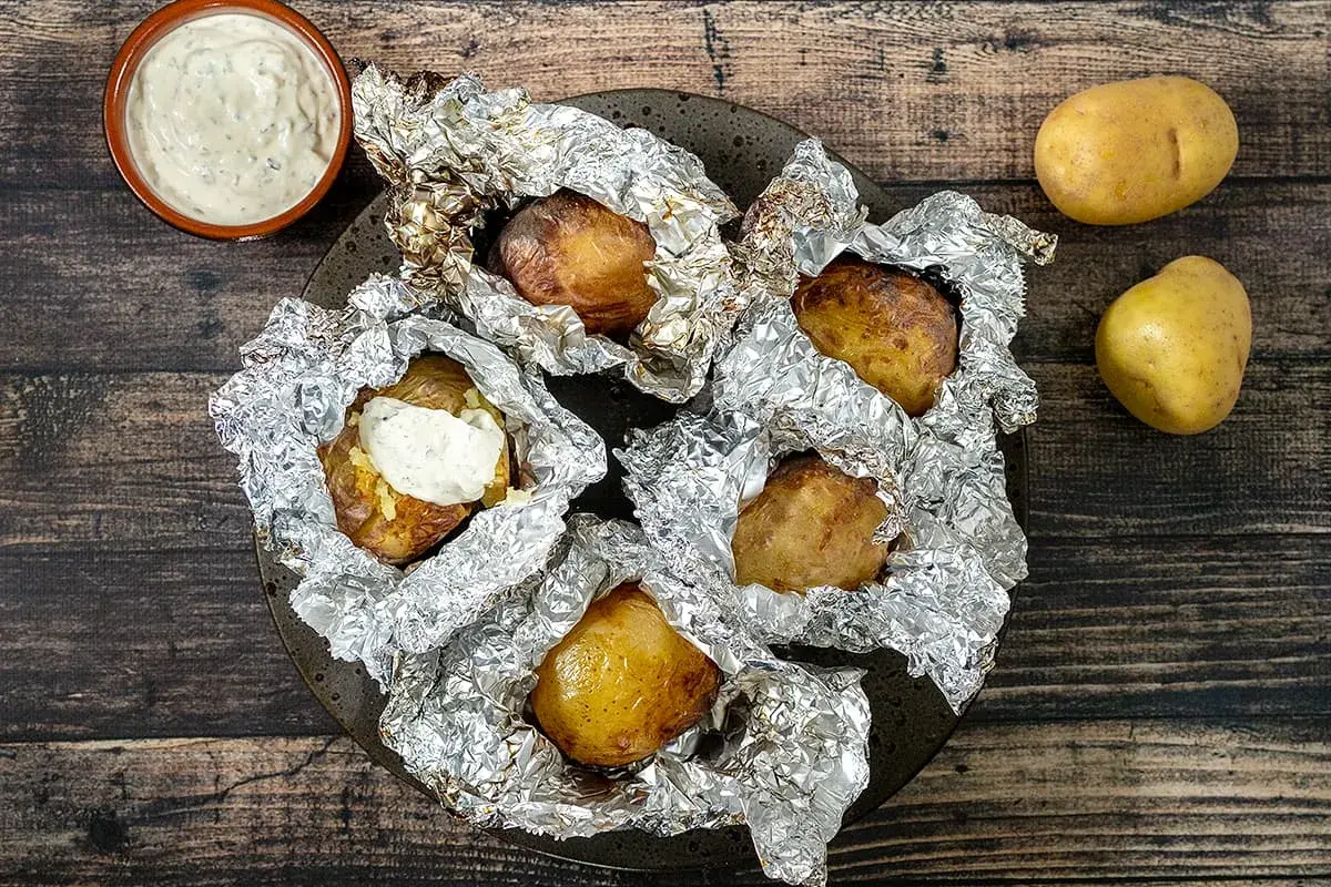 Pommes de terre en papillote sur barbecue, prêtes à être dégustées avec une sauce crémeuse. Le temps cuisson est parfait pour cette recette.