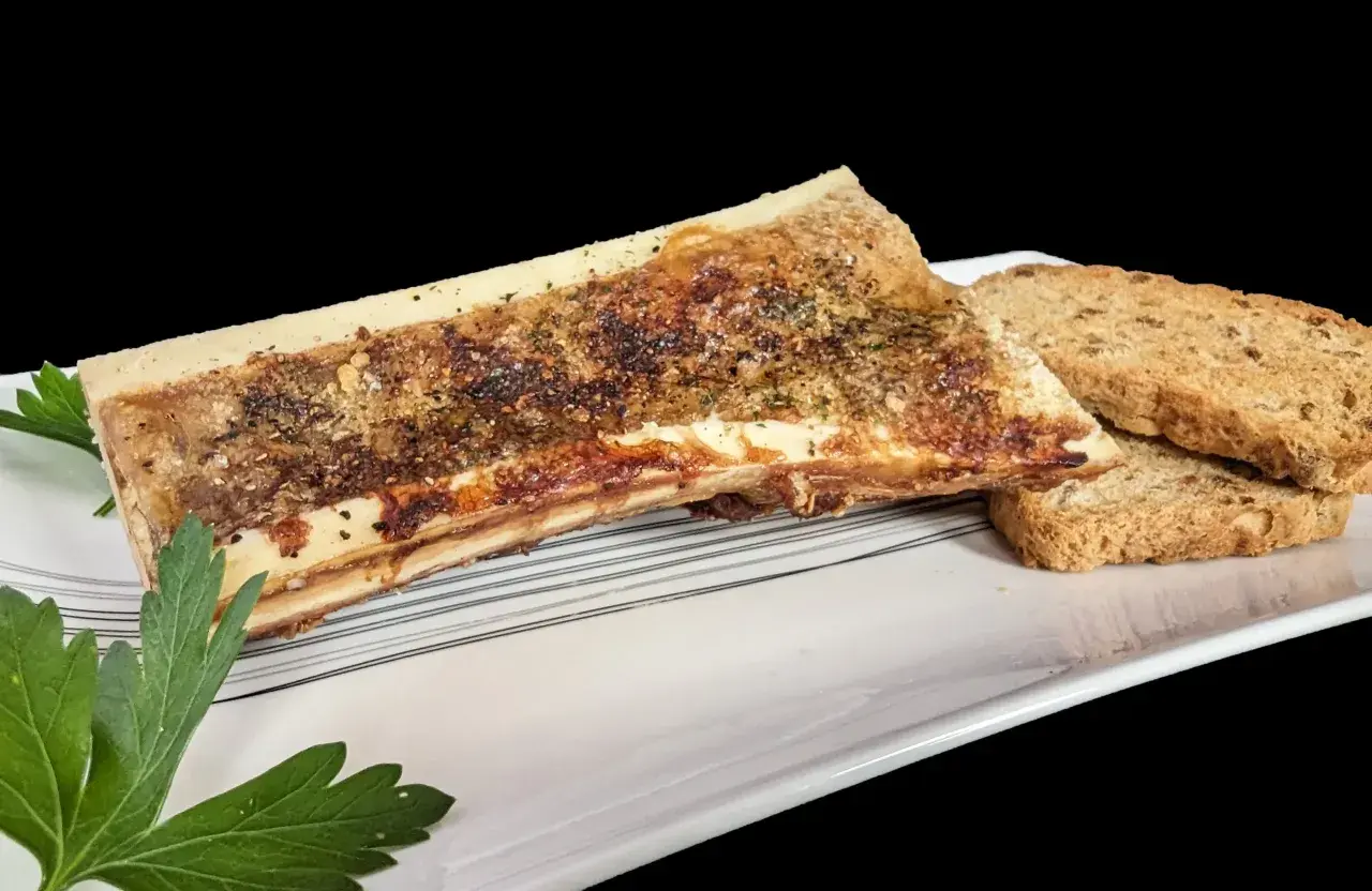 Un os à moelle rôti, assaisonné d'herbes et de poivre, servi avec des toasts croustillants sur une assiette blanche.