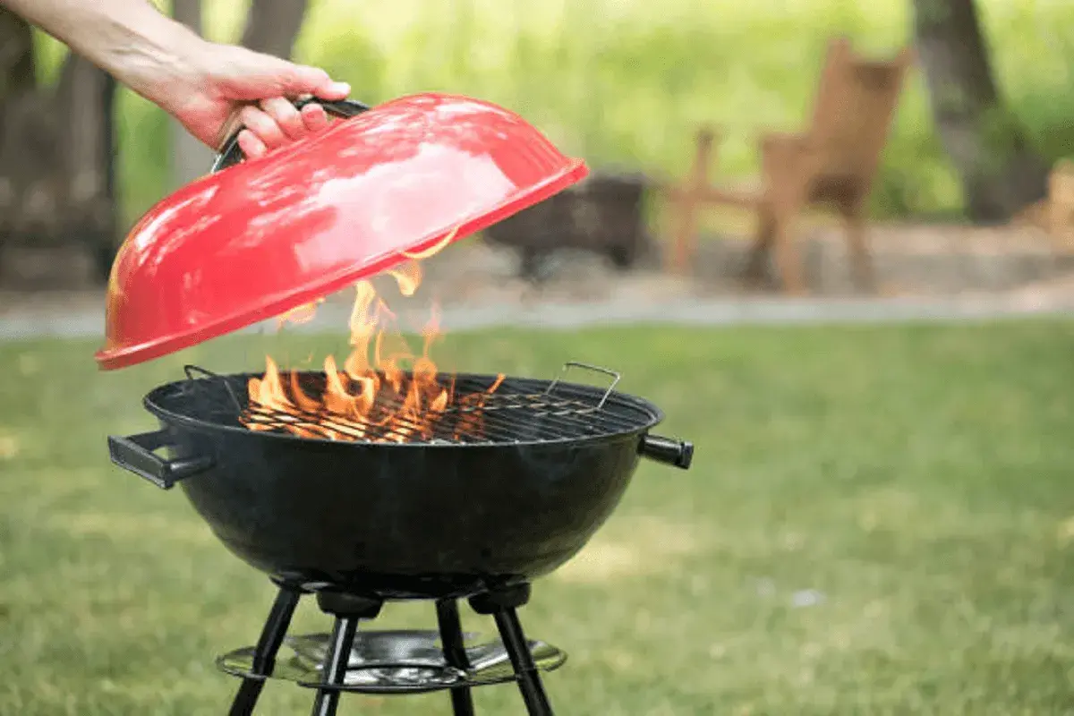 Maintenant, apprenons comment éteindre un barbecue. Une main soulève le couvercle rouge d'un barbecue noir où des flammes dansent.