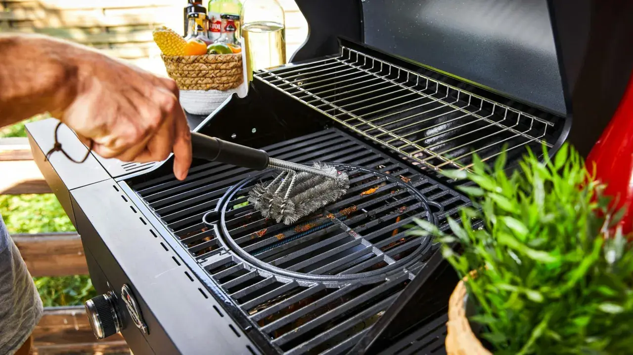 Main d'homme utilisant une brosse métallique pour nettoyer la plaque du barbecue.