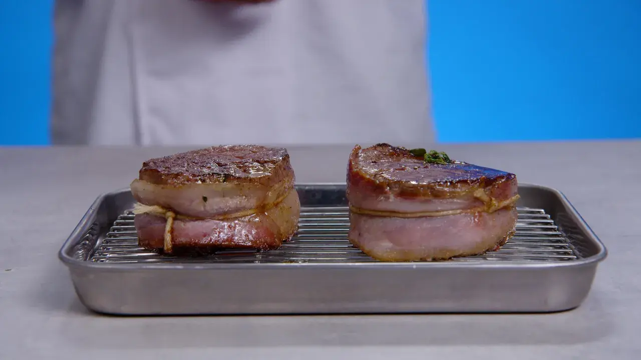 Deux filets mignons au barbecue, enveloppés de lard, reposent sur une grille dans un plat.
