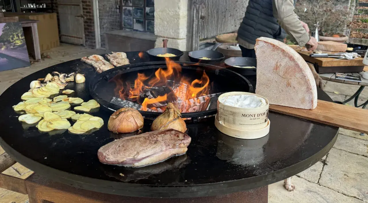 Préparation d'une recette brasero hiver : viande, pommes de terre, oignons, champignons et Mont d'Or fondent sur le feu.