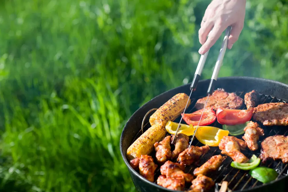 Un barbecue sain en plein air avec des épis de maïs, des poivrons colorés et des brochettes de poulet grillant sur le feu.