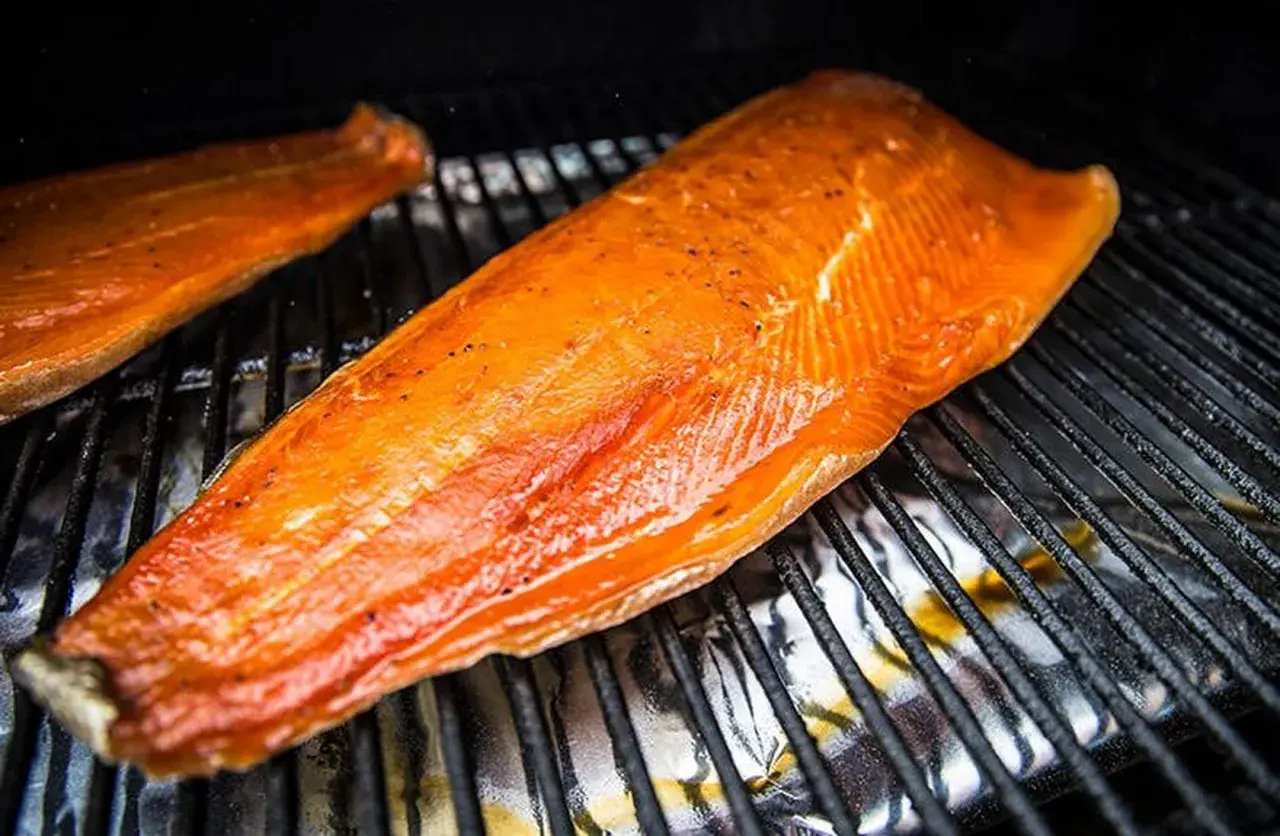 Deux filets de saumon orangés, assaisonnés de poivre, reposent sur une grille. Le temps de fumage à froid est presque terminé.