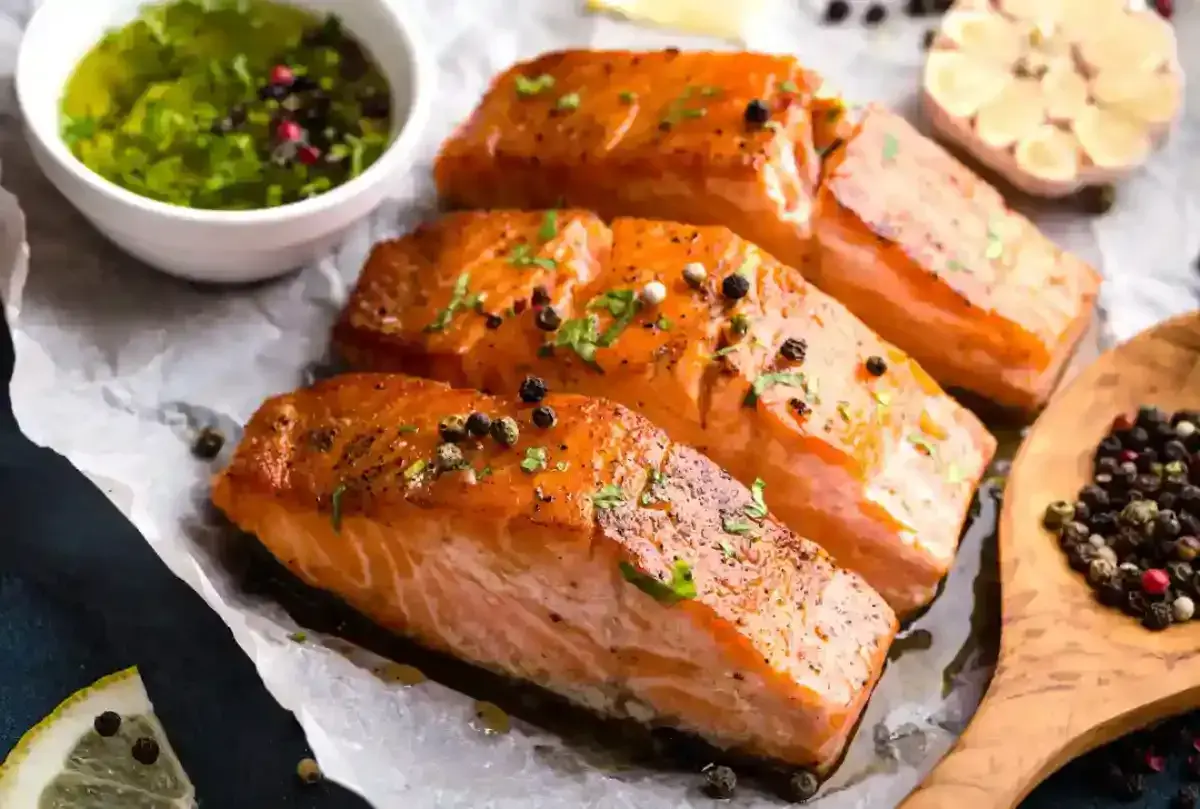 Trois pavés de saumon fumé, parsemés de poivre, accompagnés d'une sauce verte et d'une tête d'ail. Une recette parfaite pour une marinade pour saumon fumé.