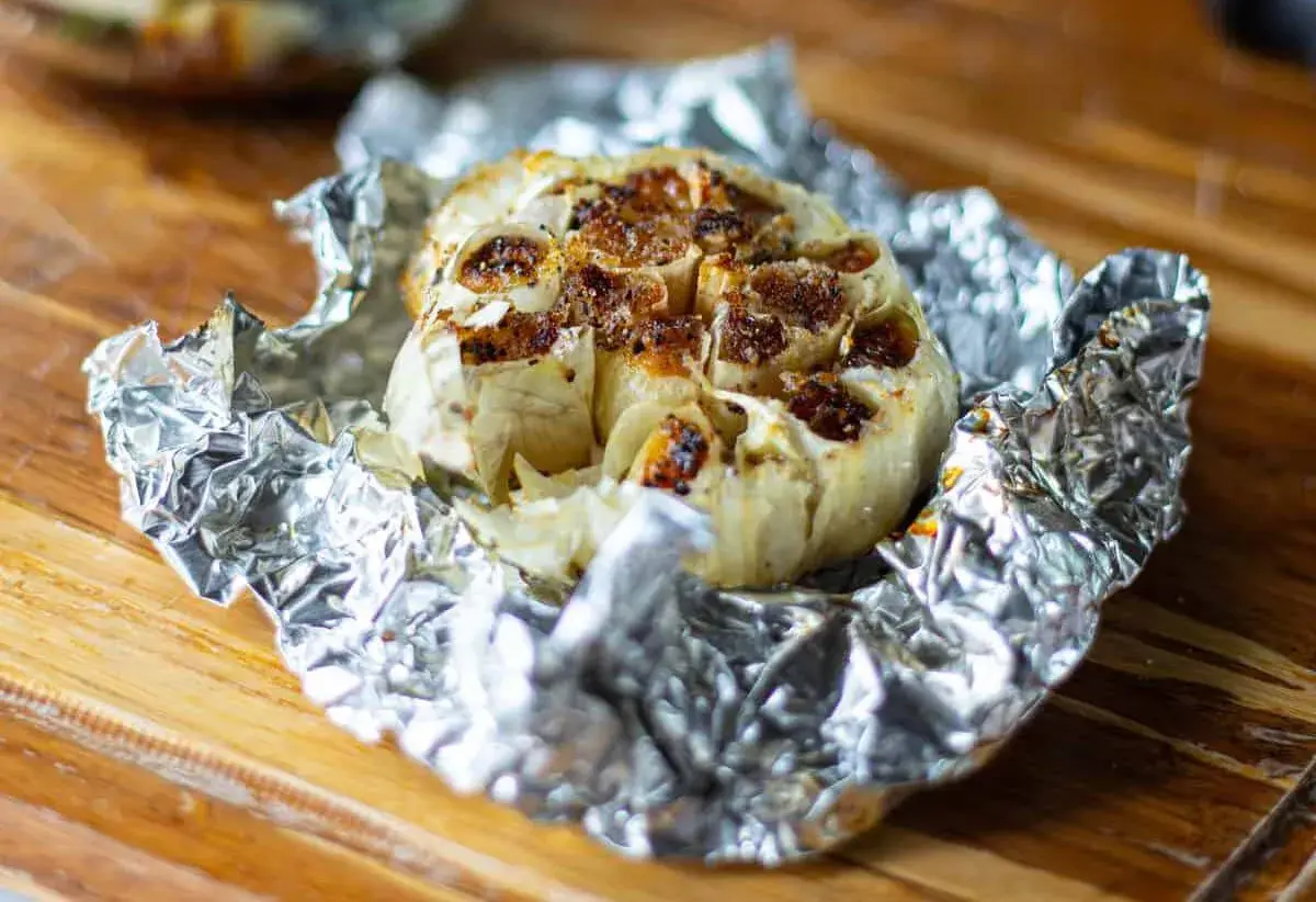 Ail au barbecue, rôti à la perfection dans du papier d'aluminium, prêt à être pressé sur du pain grillé.