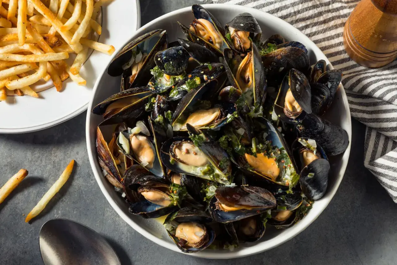Un plat généreux de moules au feu de bois, parsemées d'herbes fraîches et servies avec des frites croustillantes.