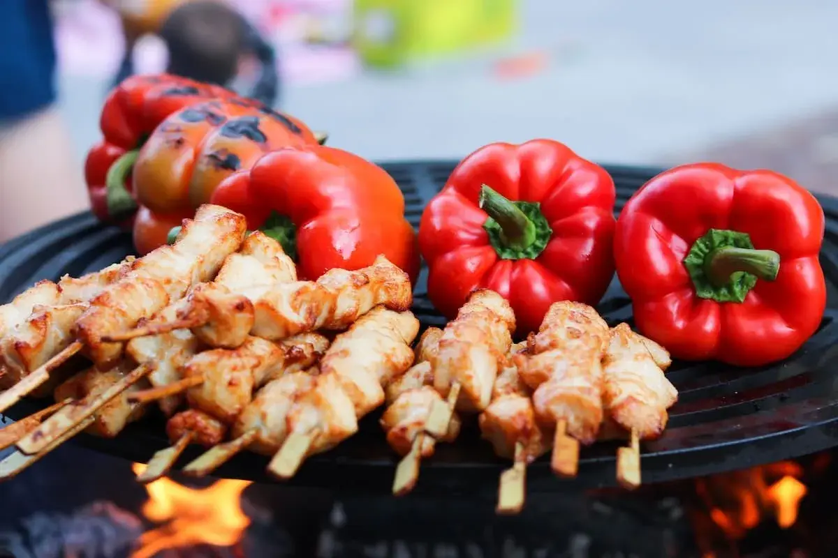 Brochettes de poulet et poivrons rouges sur un barbecue, éclairés par la lumière des flammes.