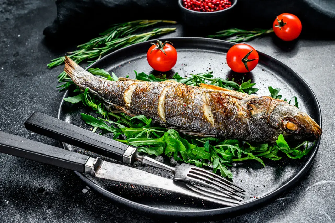 Poisson entier au barbecue, servi sur un lit de roquette avec des tomates cerises et des herbes.