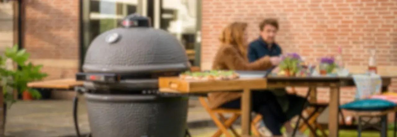 Un couple profite d'un repas en plein air avec une pizza sur une planche en bois à côté d'un barbecue kamado.