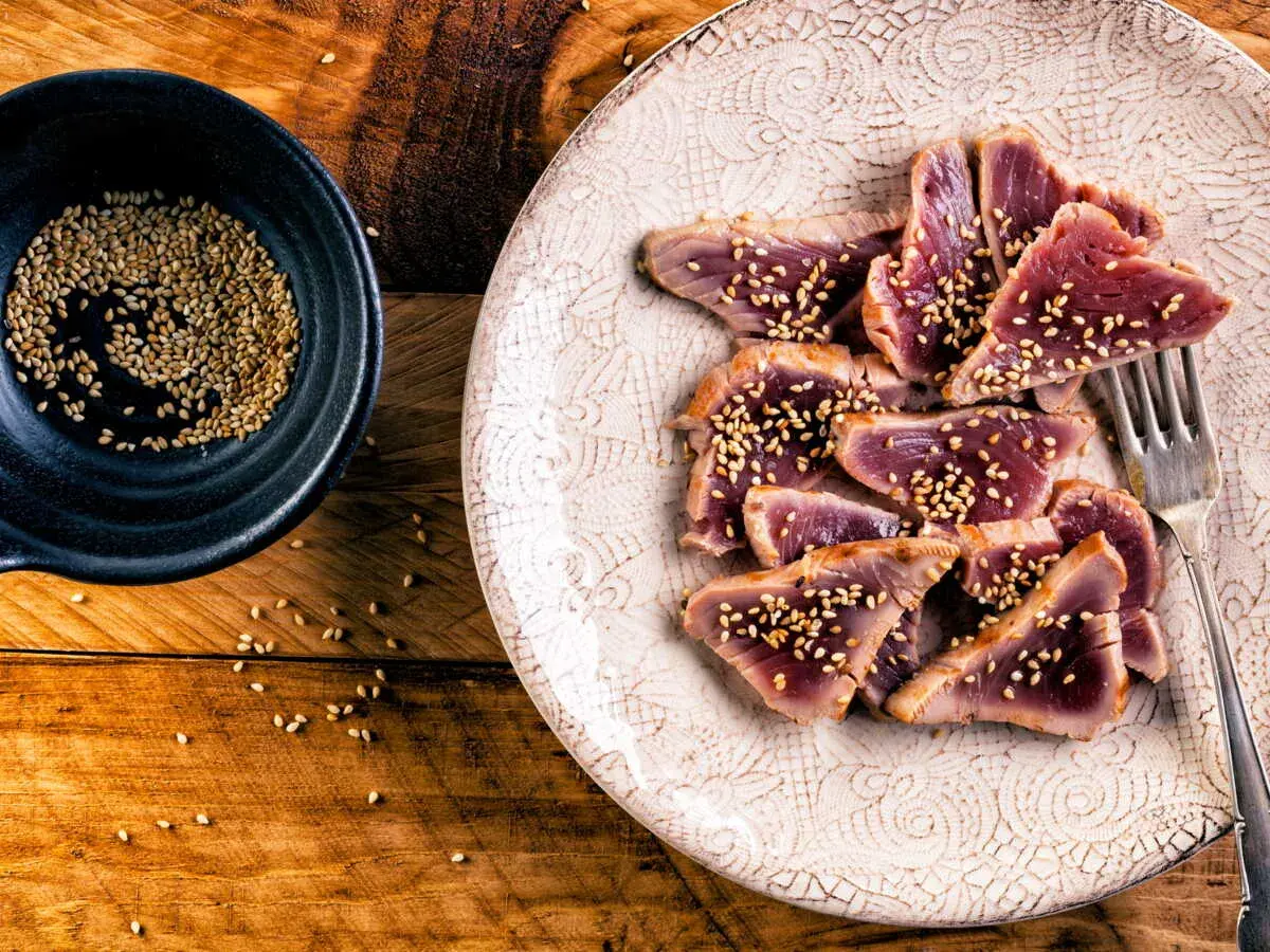 Tataki de thon, finement tranché et parsemé de graines de sésame, prêt à être dégusté. Une assiette élégante sur fond de bois rustique.