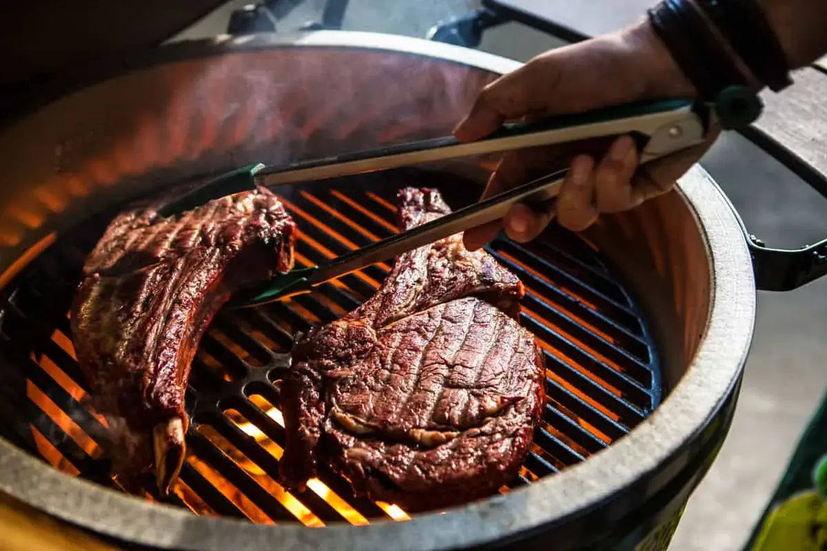 Deux côtes de bœuf savoureuses sur un barbecue à gaz, prêtes pour le temps de cuisson idéal. La chaleur intense des flammes caramélise la viande.