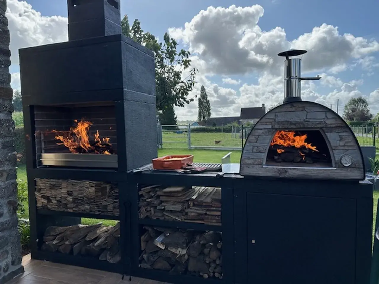 Un grand barbecue et un four à pizza en pierre sont prêts à preparer barbecue. Le feu crépite dans les deux, promettant un repas convivial en plein air.