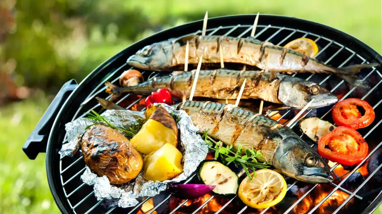 Trois poissons maquereaux grillés sur un barbecue, accompagnés de pommes de terre en papillote, de tomates et de citrons. Un délice de poisson barbecue en plein air.