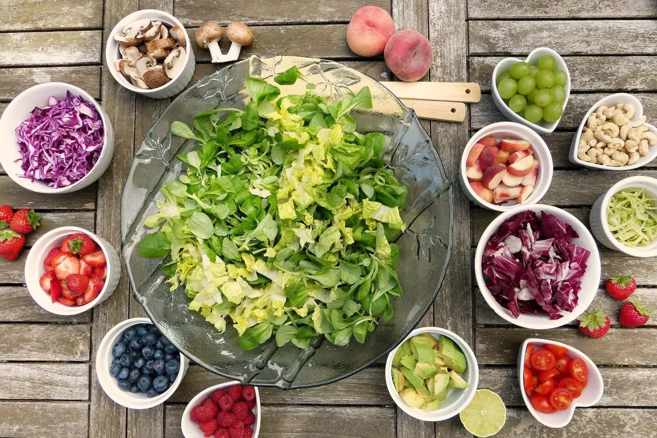 Préparation d'une salade barbecue : laitue, chou rouge, fraises, myrtilles, framboises, avocat, tomates cerises, pêches, raisins, noix de cajou, champignons et chou vert.