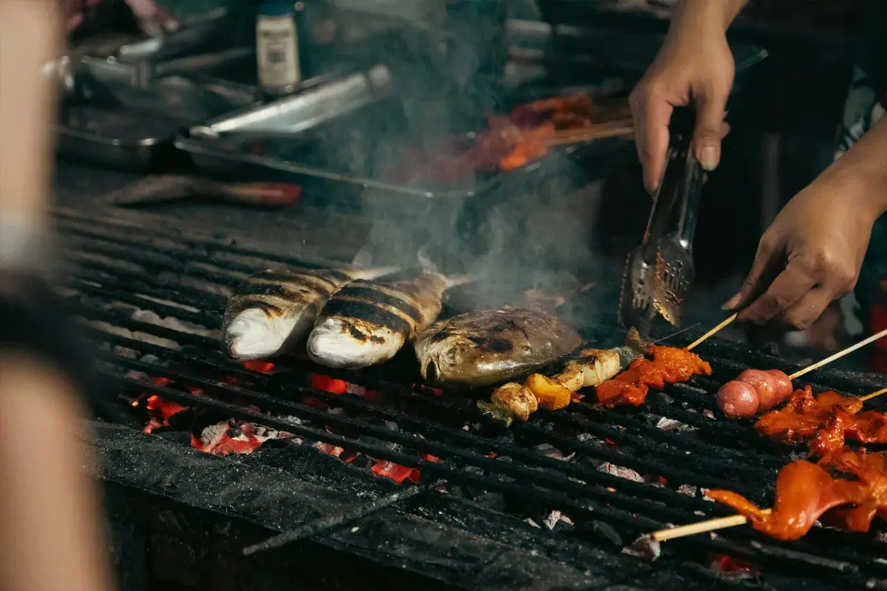 Poissons et brochettes marinés cuisent sur un gril incandescent, dégageant une fumée alléchante. Un vrai bar au barbecue !