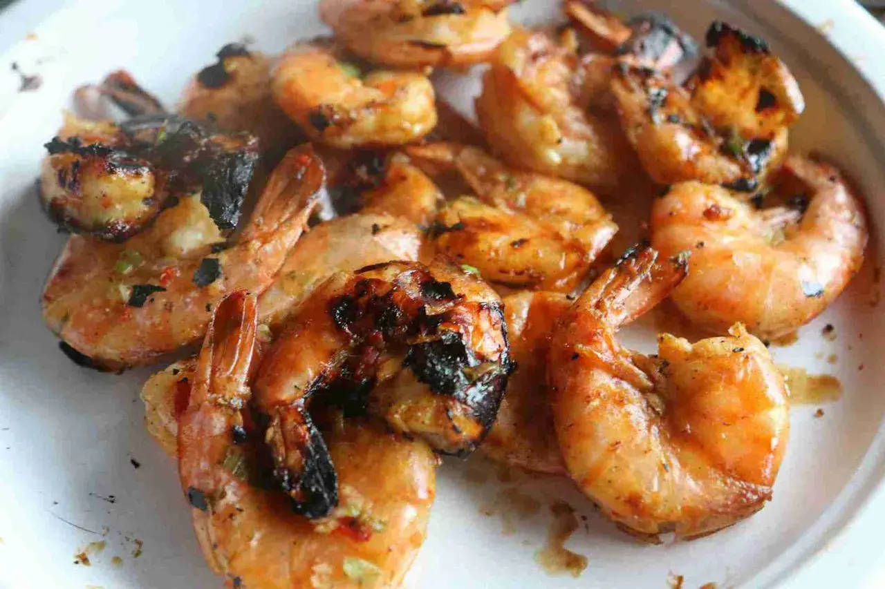 Grosses crevettes bbq, grillées à la perfection, avec des marques de cuisson foncées et une sauce savoureuse.