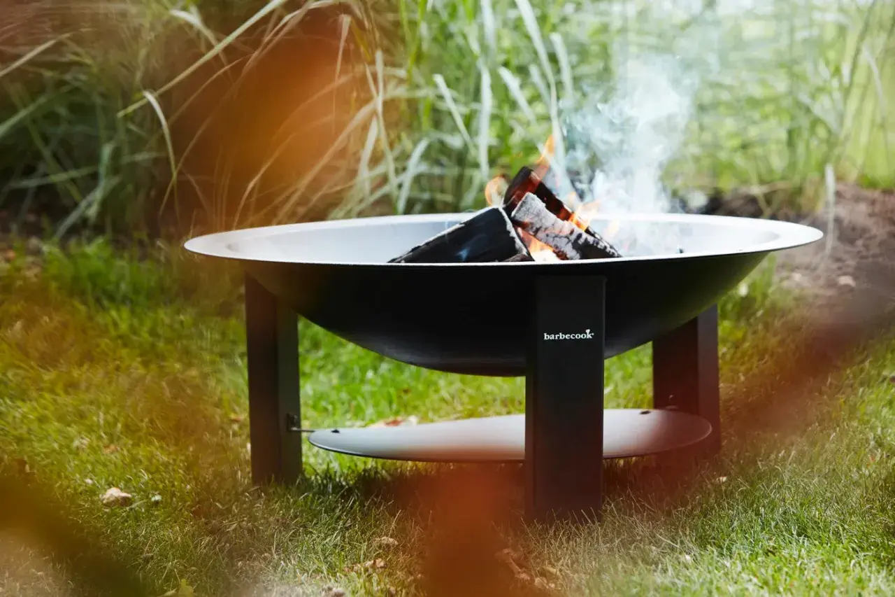 Un brasero Barbecook est prêt à allumer, avec des flammes dansantes et de la fumée s'élevant dans l'air.