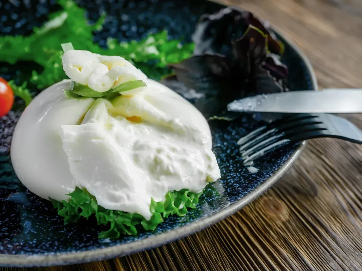 Une burrata fumée onctueuse sur un lit de verdure, prête à être dégustée. Une recette simple et savoureuse.