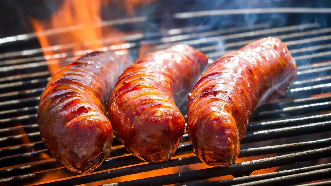 Trois saucisses de bœuf grillent sur un barbecue, leurs jus pétillent sous les flammes. La cuisson saucisse de bœuf barbecue est à son apogée.