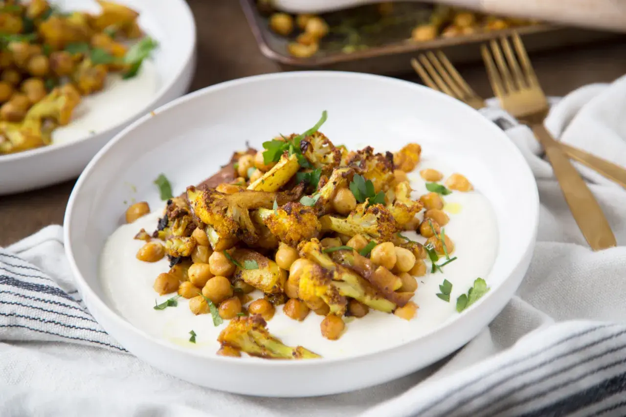 Chou-fleur rôti aux épices, pois chiches et sauce crémeuse. Un délice de chou fleur barbecue, garni de persil frais.