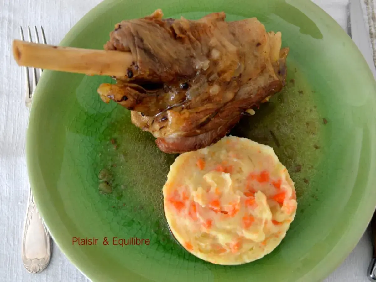Souris d'agneau confite, tendre et savoureuse, servie avec une purée de carottes onctueuse sur une assiette verte craquelée.
