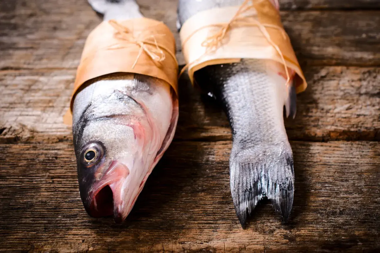 Deux poissons prêts pour le barbecue, emballés dans du papier kraft sur une table en bois rustique.