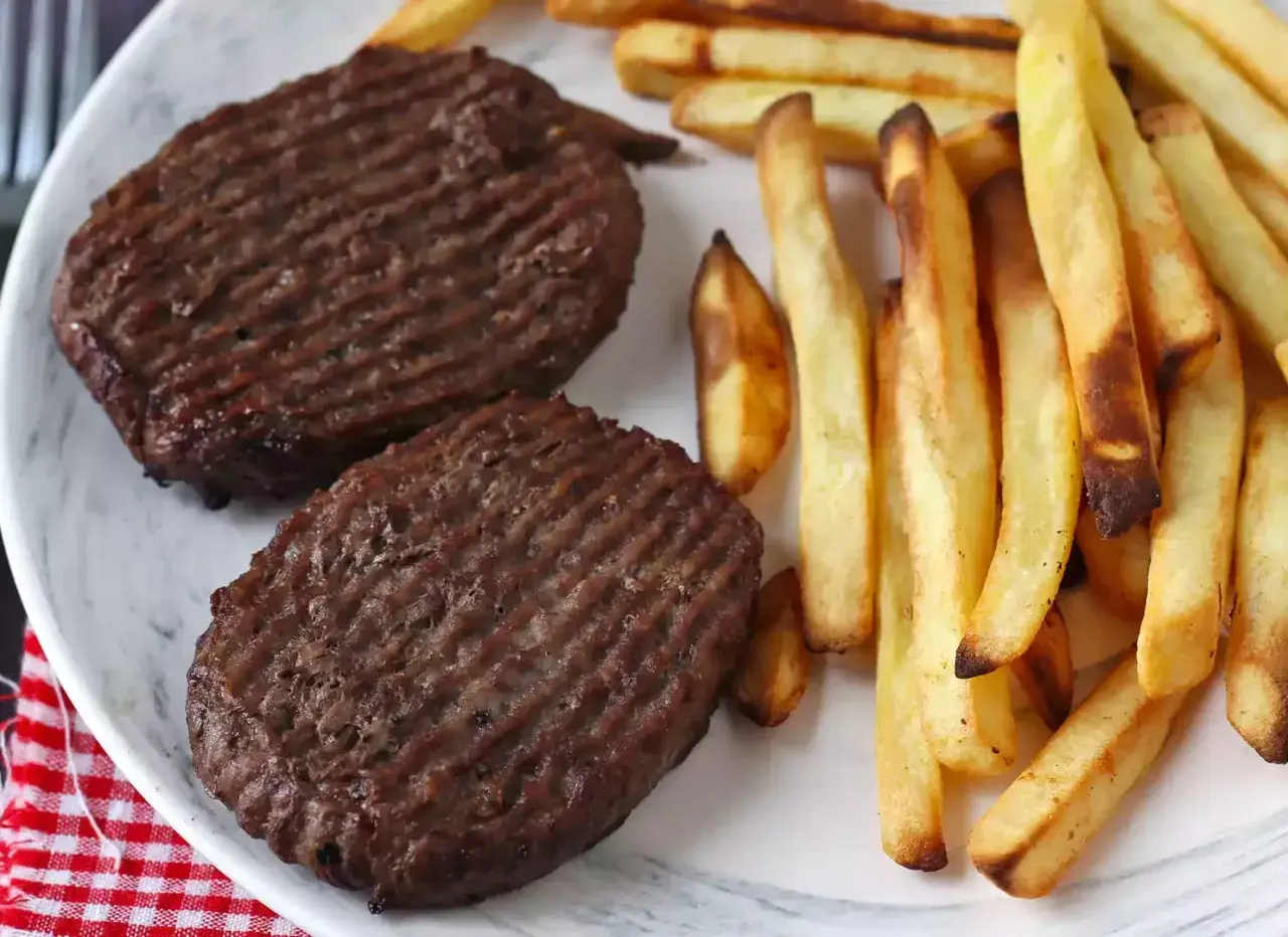 Deux steaks hachés au grill électrique, marqués de fines rayures, accompagnés d'une généreuse portion de frites dorées et croustillantes.