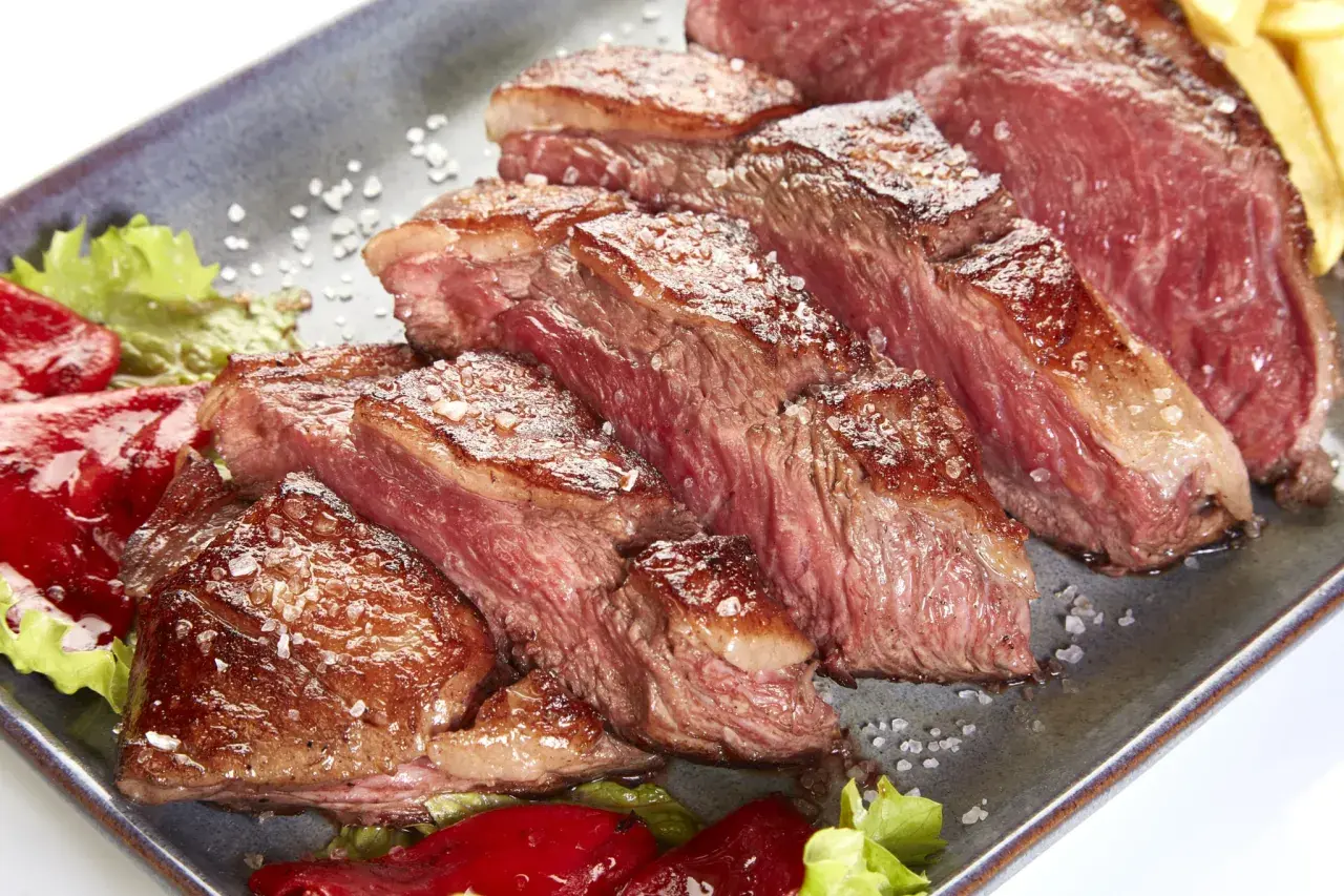 Tranches de picanha de veau juteuse, saupoudrées de gros sel, servies avec des poivrons rouges et de la laitue.