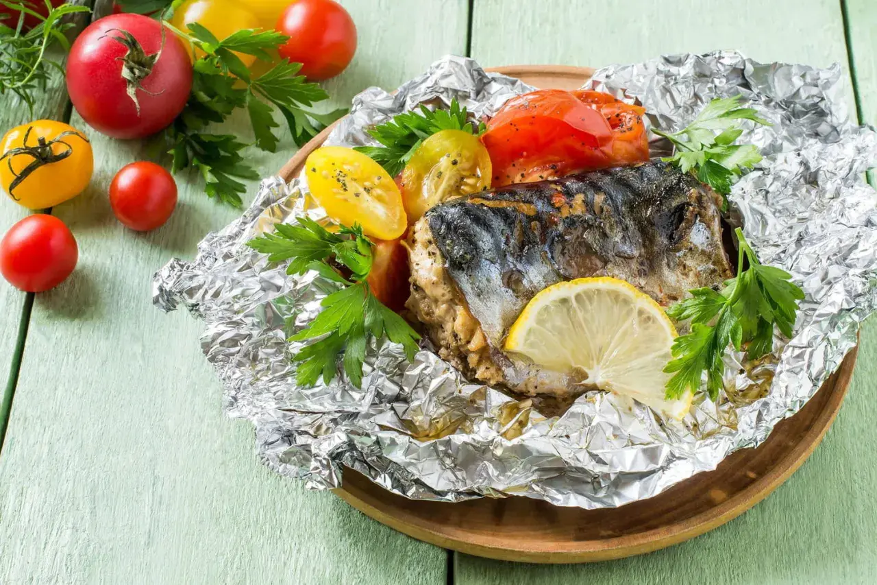 Poisson barbecue en papillote, servi avec des tomates et du persil, garni d'une tranche de citron.