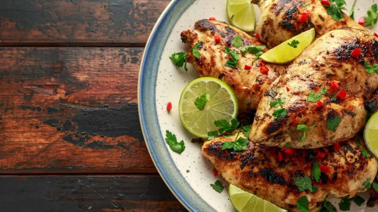 Poulet grillé, garni de coriandre fraîche, de piment rouge et de quartiers de citron vert, évoquant une savoureuse marinade mexicaine.