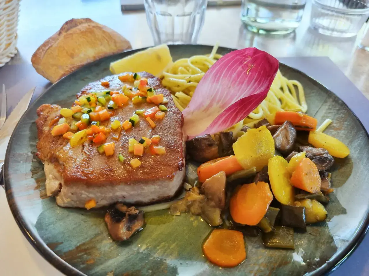 Pavé de thon poêlé, garni de dés de légumes croquants, servi avec des pâtes, des légumes racines et une feuille de chicorée. Une recette savoureuse.
