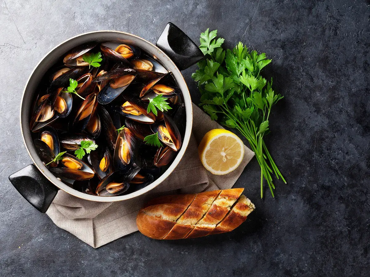 Un plat de moules grillées, garni de persil frais, d'un quartier de citron et d'une baguette à l'ail, prêt à être dégusté.