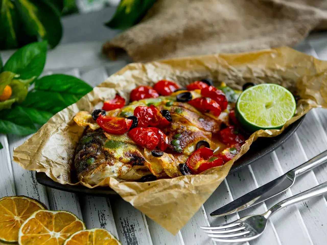 Dorade en papillote au barbecue, garnie de tomates cerises, olives et citron vert. Le temps de cuisson est parfait pour ce plat savoureux.