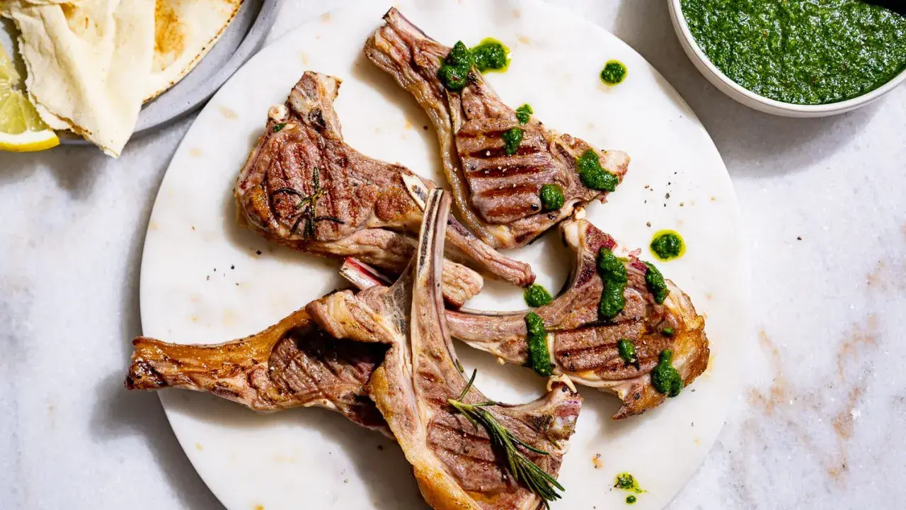 Délicieuses côtelettes d'agneau barbecue, grillées à la perfection, arrosées d'une sauce verte vibrante et garnies de romarin frais.