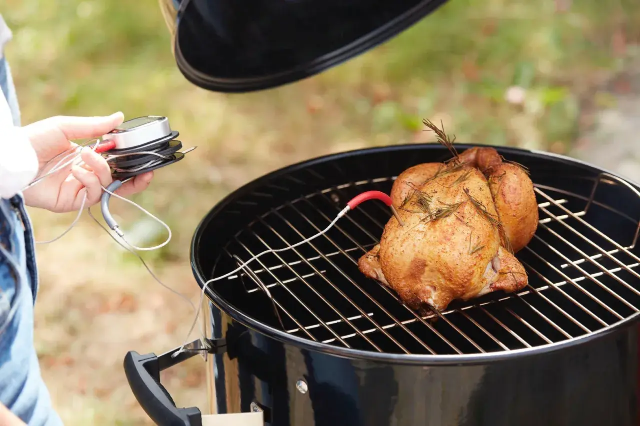 Un poulet fumé, doré et savoureux, est sur le gril. Une sonde de température est insérée pour une cuisson parfaite.