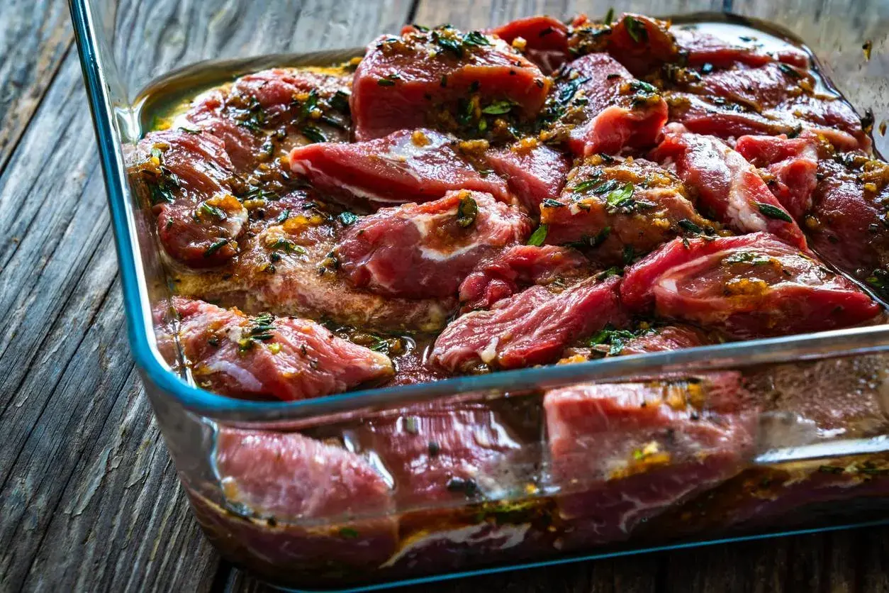 Morceaux de joue de porc marinés dans un plat en verre, prêts à être cuisinés.