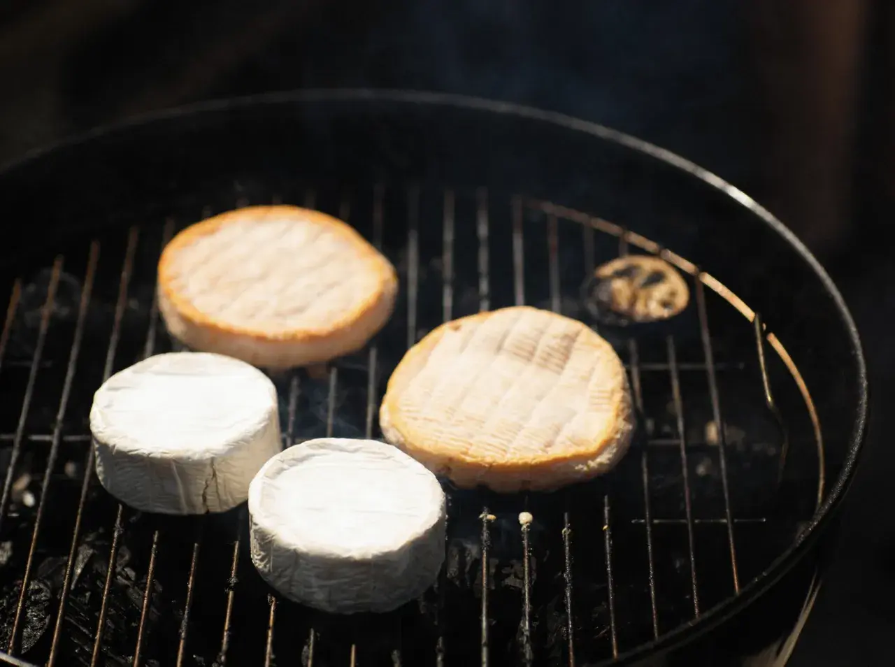 Fromages ronds, dont certains enrobés de blanc, chauffent sur un barbecue. Une idée gourmande pour un barbecue feta.
