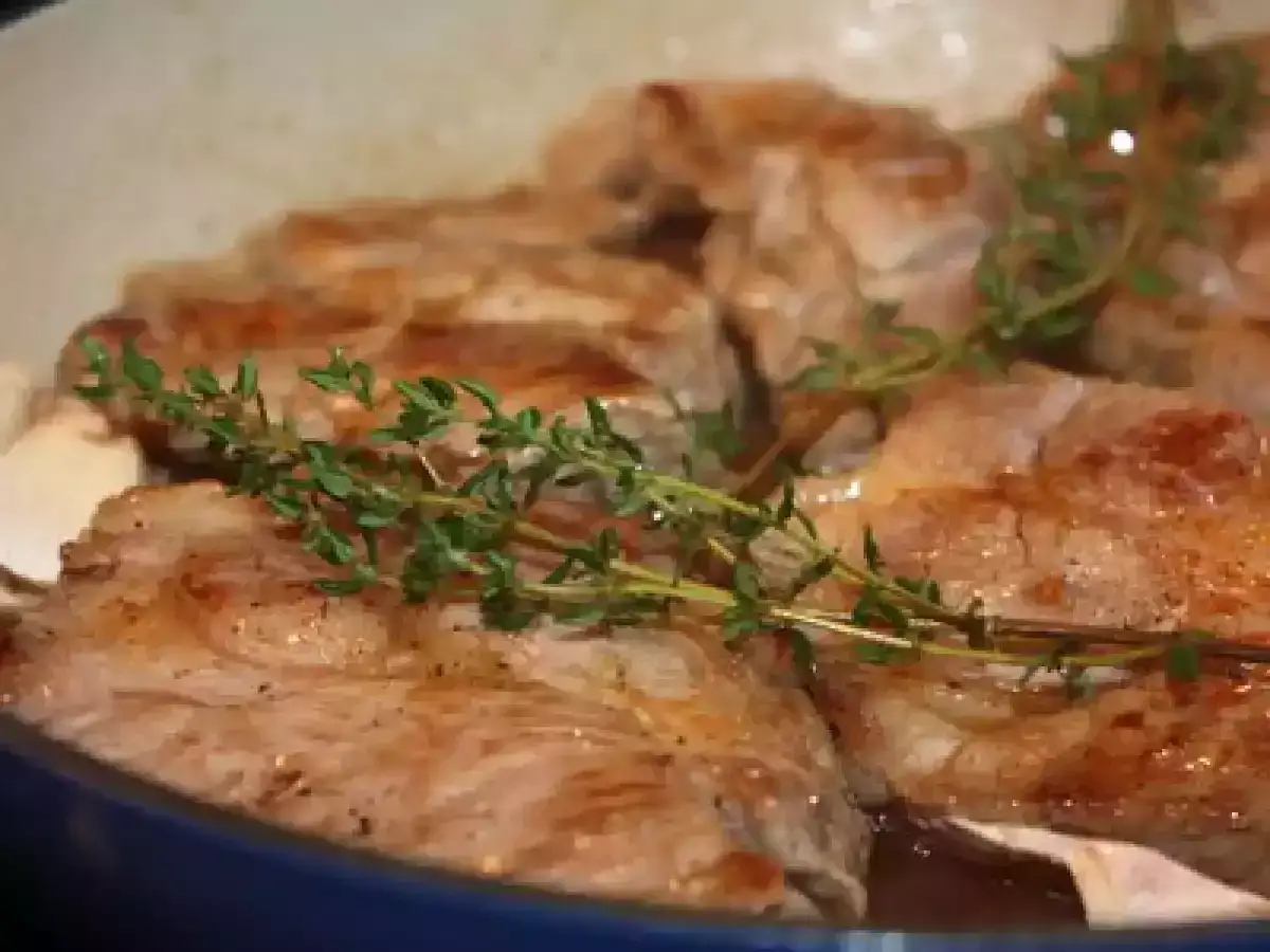 Tranches d'&eacute;chine de porc dor&eacute;es dans une po&ecirc;le, garnies de brins de thym frais.